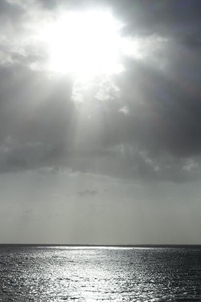 A photo of the ocean during cloudy weather. The sun is breaking through the clouds, illuminating the water surface in a particular spot, creating a divine vibe.