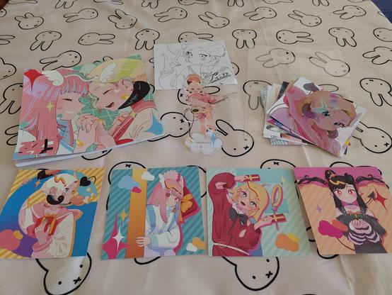 Photo of an artbook, an acrylic stand and various CD-sized cards featuring various anime/manga style characters.